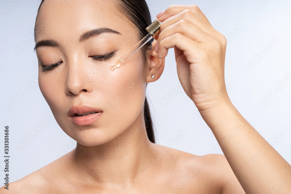 Asian beautiful female is applying eye serum