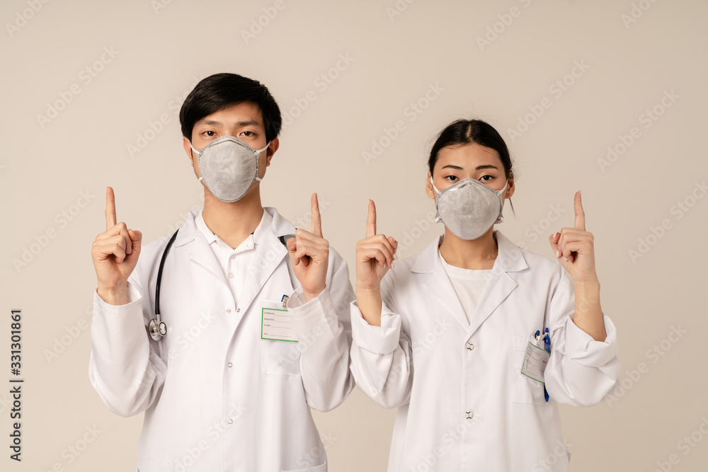Image of asian young doctors in protective masks pointing fingers upward