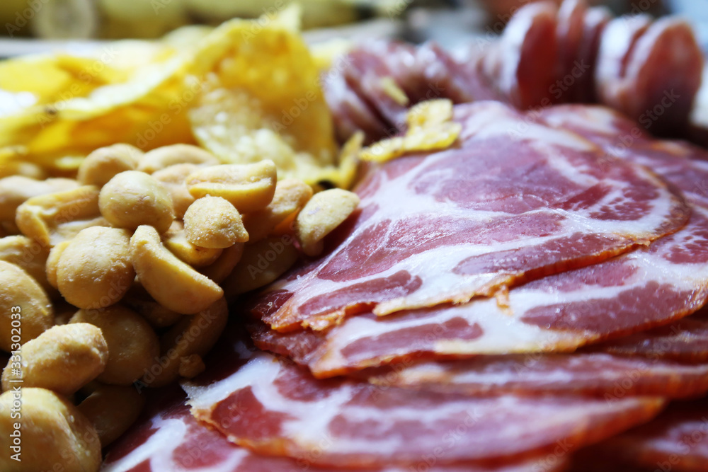 Close-up of a snacks platter with salami, jamon, peanuts and potato chips