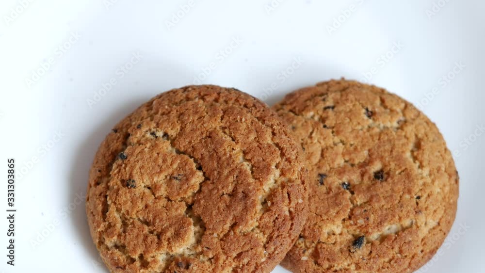 Oatmeal cookies are lie on white plate. Male hand takes sweet ruddy cookie one by one. Concept of overeating and abuse of carbohydrate-rich foods. Glycemic foods that increase blood insulin levels Oatmeal cookies are lie on white plate. Male hand takes sweet ruddy cookie one by one. Concept of overeating and abuse of carbohydrate-rich foods. Glycemic foods that increase blood insulin levels