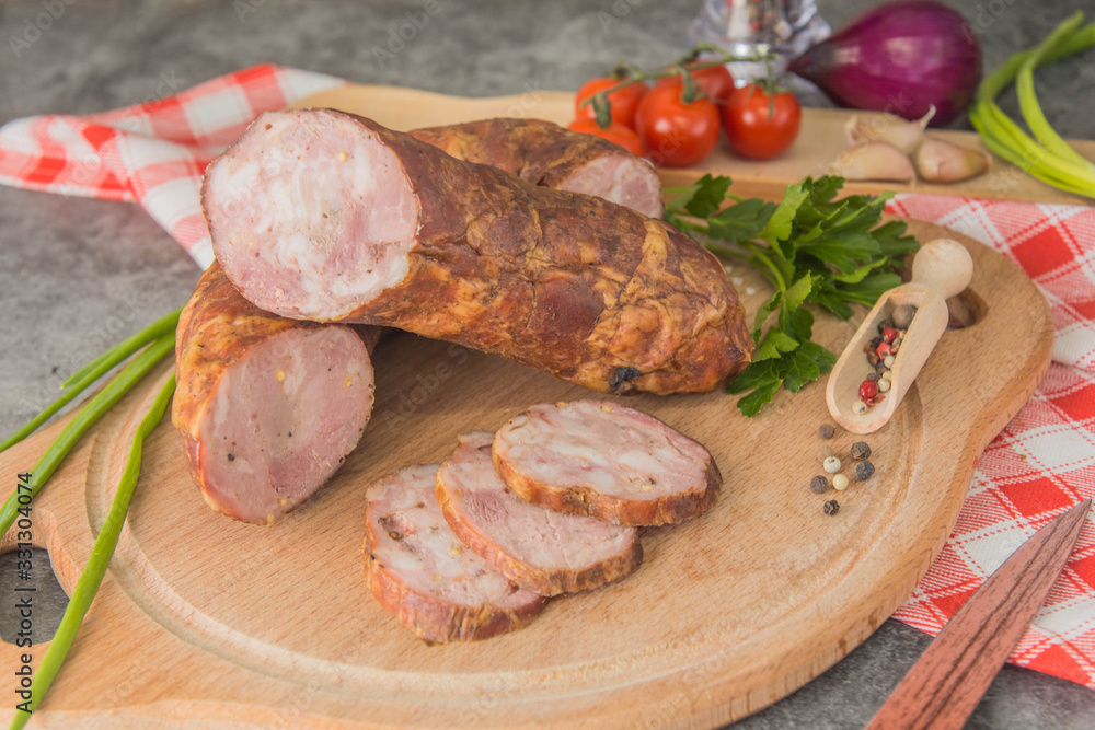 Sausage with minced meat, cut into small pieces on a wooden board with spices and herbs. Close-up