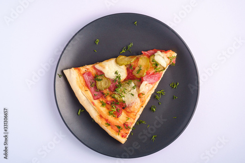 Pizza slice with pepperoni, salami, melted mozzarella cheese, pickles and dill in black plate on white background, top view copy space