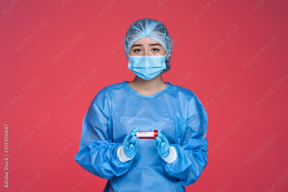 chinese woman doctor in special costume holding test tube with blood sample. Covid-19 positive test. On red background chinese woman doctor in special costume holding test tube with blood sample. Covid-19 positive test. On red background