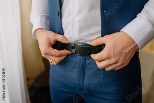 A man, groom buttoned a black leather trouser belt. Groom dress up a belt with buckle. Businessman wear leather stylish belt.
