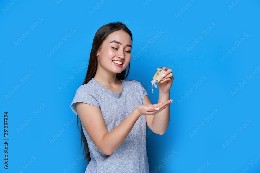 Young Chinese woman disinfecting hands with antiseptic on blue background Young Chinese woman disinfecting hands with antiseptic on blue background