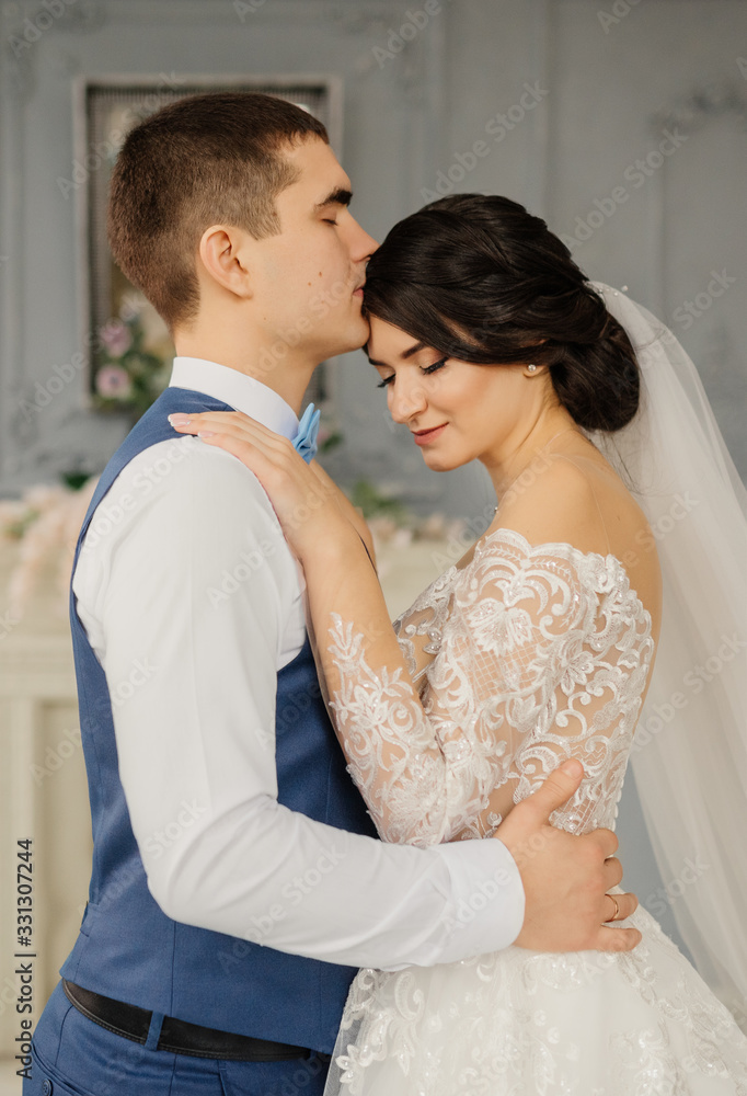 Happy groom kisses the bride hugging her waist in a vintage interior. Beautiful elegant couple of newlyweds in love. Wedding concept. Happy newlywed couple.