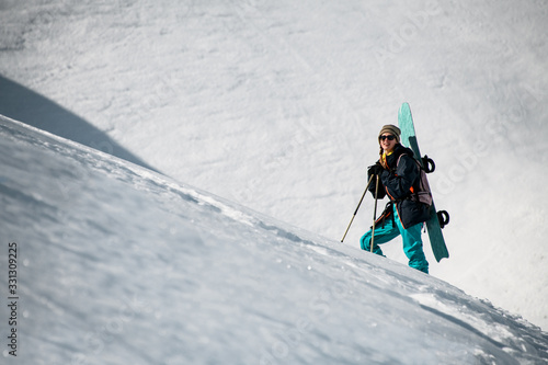 Female hiker goes up the mountain with snowboard