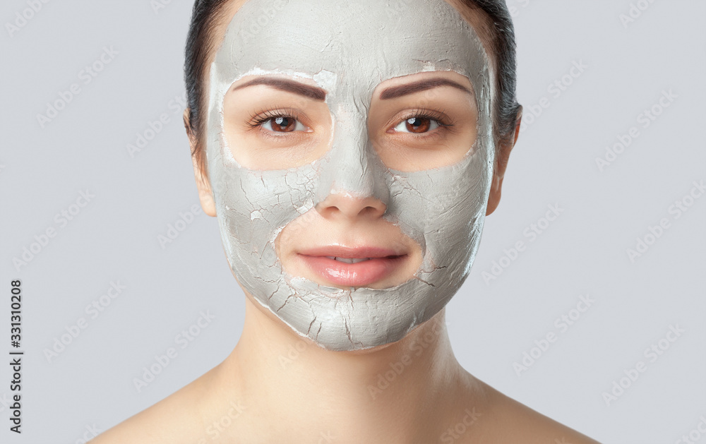 Beautician makes a face clay mask against acne on the face of a woman to rejuvenate the skin. Cosmetology treatment of problem skin on the face and body. Beautician makes a face clay mask against acne on the face of a woman to rejuvenate the skin. Cosmetology treatment of problem skin on the face and body.