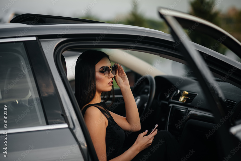 Stylish young girl sitting in a business class car in a black dress. Business fashion and style