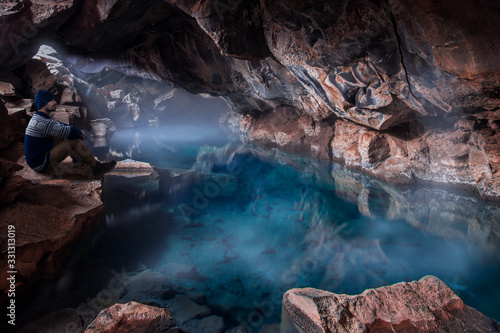 man sitting in cave with blue geothermal pool