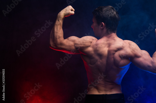 Muscular man showing muscles isolated on the black background with colored smoke. Concept of healthy lifestyle 