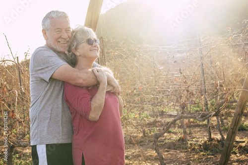 Cheerful couple of happy active senior caucasian man and woman couple - mature retired people in outdoor leisure activity in wine yard with sunlight in background - concept of together forever photo