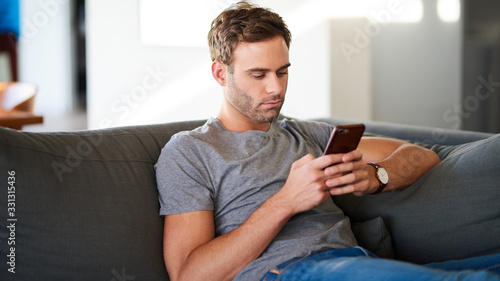 Young man texting while sitting on his living room sofa