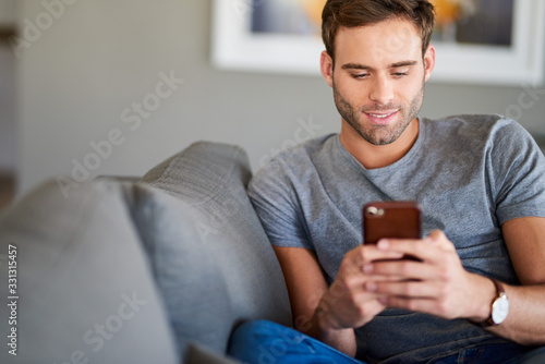 Smiling young man texting on his living room sofa
