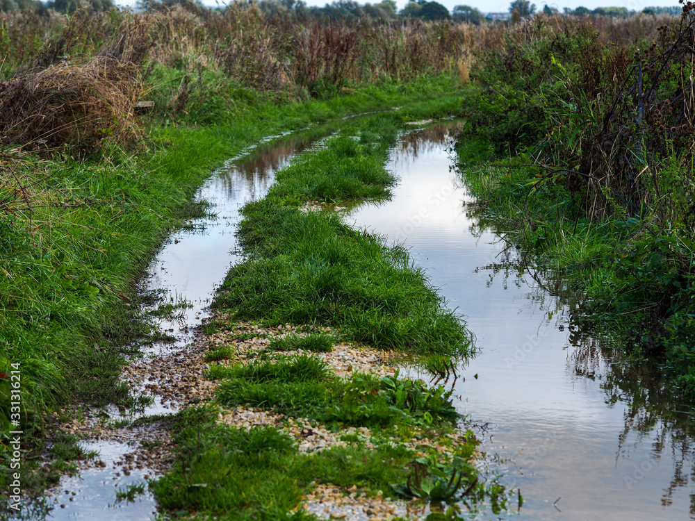 Flooded grassy country lane with the sky reflected in standing water at Wheldrake Ings, North Yorkshire, England