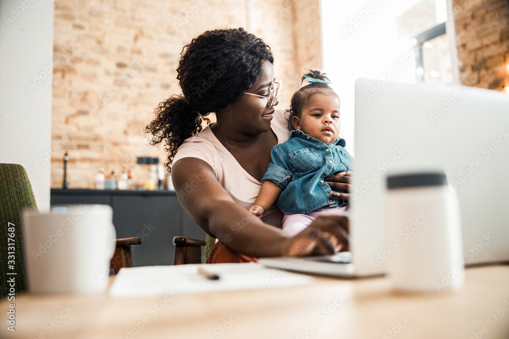 Smiling Afro American lady holding baby girl and using laptop Smiling Afro American lady holding baby girl and using laptop