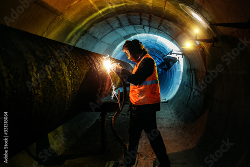 Obraz na płótnie Worker in protective mask welding pipe in tunnel