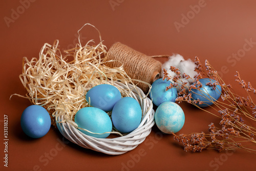Dyed easter eggs in the nest and cotton flowers an a brown background. Easter card with blue decorated eggs in a rustic style.
