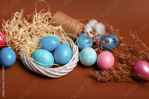 Dyed easter eggs in the nest and cotton flowers an a brown background. Easter card with blue decorated eggs in a rustic style.