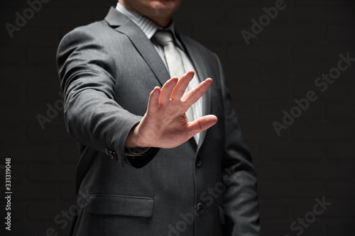businessman portrait showing palm of hand, dressed in gray suit, dark wall background