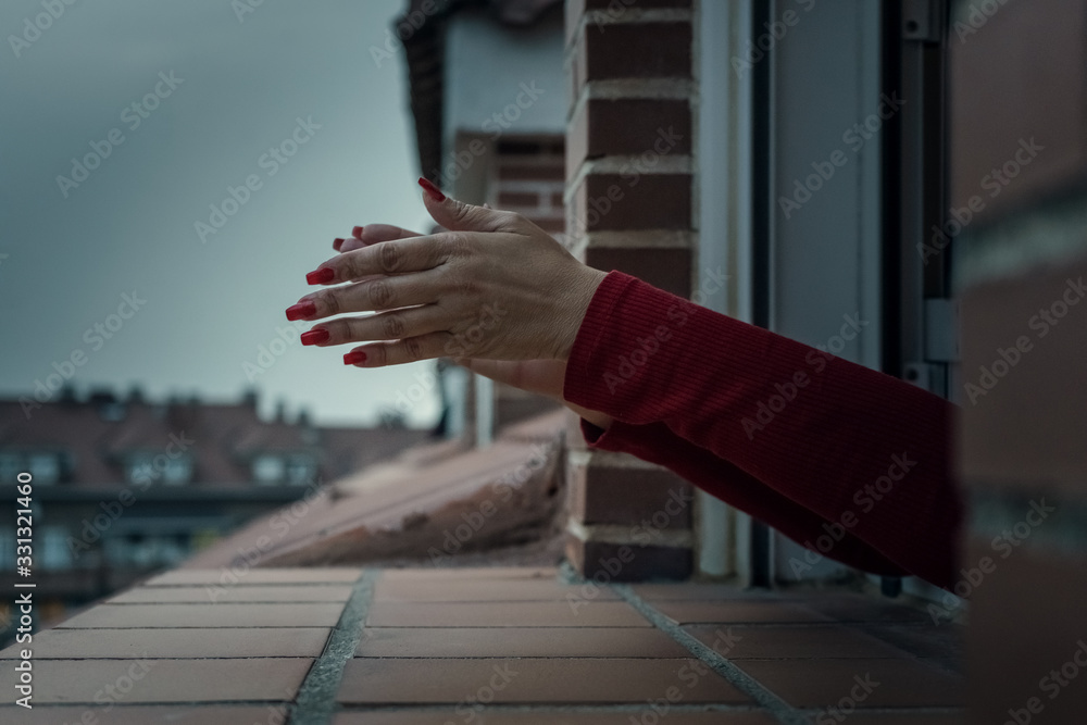a woman's hands with red nails sticking out the window to clap. coronavirus quarantine