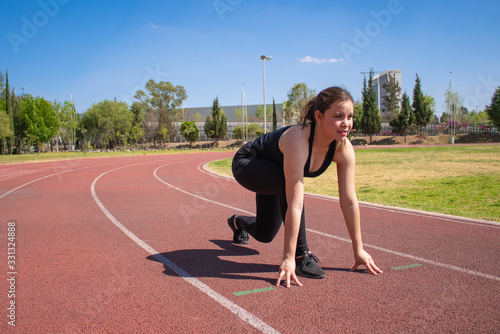 Mujer Fitness con ropa negra en pista de tartán preparándose para correr durante un día soleado