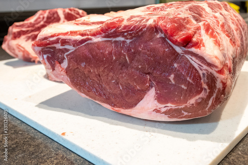 A close up of a large prime rib roast which is sitting on a white plastic cutting board. The meat has some marbling and multiple ribs. There's a small roast in the background.