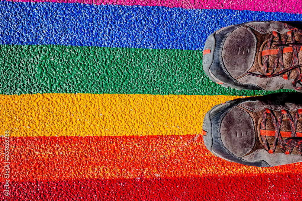 © Road Red Runner - A man steps on his boots with the gay flag, painted on the ground, a concept of contempt for rights.