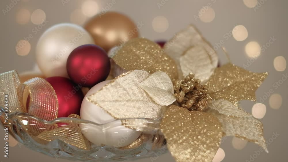 Christmas composition in golden, white and red tones with Poinsettia flower and baubles in glass candy dish. 4K resolution trucking shot. Shallow depth of field. Christmas composition in golden, white and red tones with Poinsettia flower and baubles in glass candy dish. 4K resolution trucking shot. Shallow depth of field.