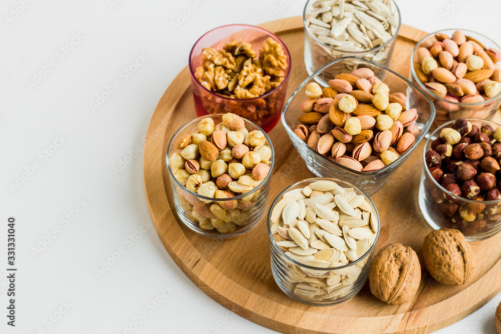Shelled nuts varieties with walnuts,hazelnuts,pistachio,almonds and seeds in glass bowls on wooden tray,half view Shelled nuts varieties with walnuts,hazelnuts,pistachio,almonds and seeds in glass bowls on wooden tray,half view