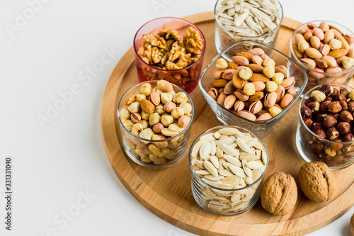 Shelled nuts varieties with walnuts,hazelnuts,pistachio,almonds and seeds in glass bowls on wooden tray,half view