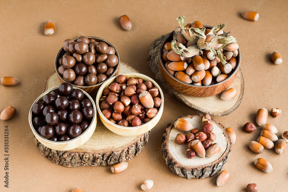 Milky and dark chocolate covered hazelnuts in bamboo bowls on wooden table with natural hazelnuts. Milky and dark chocolate covered hazelnuts in bamboo bowls on wooden table with natural hazelnuts.