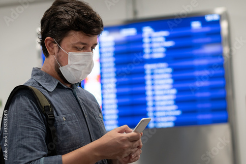 Traveler man looks at cell phone in front of flight panel. Coronavirus epidemic photo