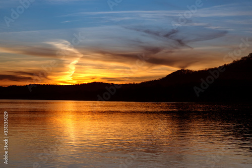 The sunset paints the sky over the hills of the Ohio River Valley with the reflection of fading evening light upon the calm water as photographed from the West Virginia shore.