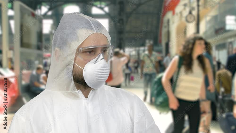 Portrait of man in white protective clothing and respiratory mask. Crowded airport terminal or railway station on background. Portrait of man in white protective clothing and respiratory mask. Crowded airport terminal or railway station on background.