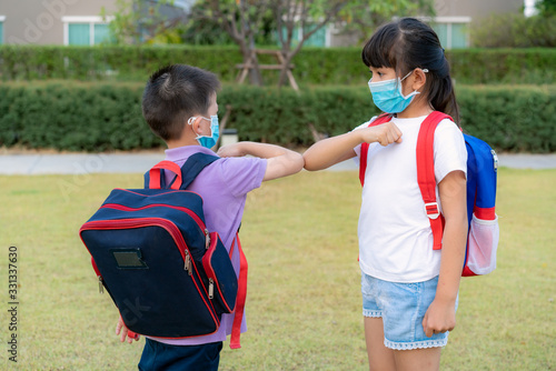 Elbow bump is new novel greeting to avoid the spread of coronavirus. Two Asian children preschool friends meet in park. Instead of greeting with a hug or handshake, they bump elbows instead.