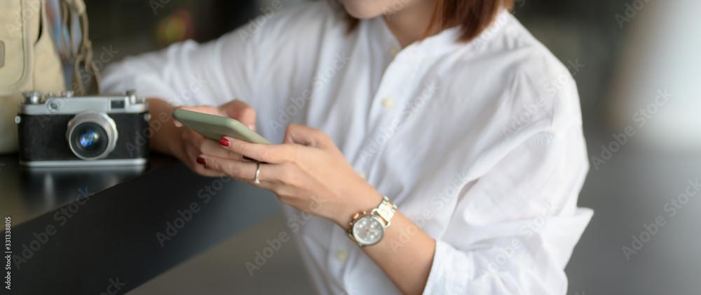 Fototapeta premium Close up view of young female photographer working with smartphone and camera