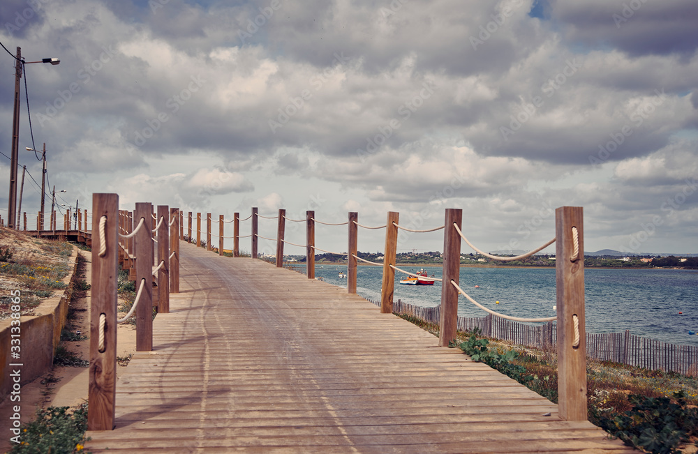 Fototapeta premium Algarve Faro coastline view. Wooden pathway, blue cloudy sky