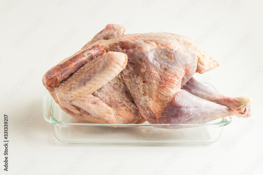 Frozen,cleaned and uncooked turkey in the glass oven container on the white surface. Frozen,cleaned and uncooked turkey in the glass oven container on the white surface.