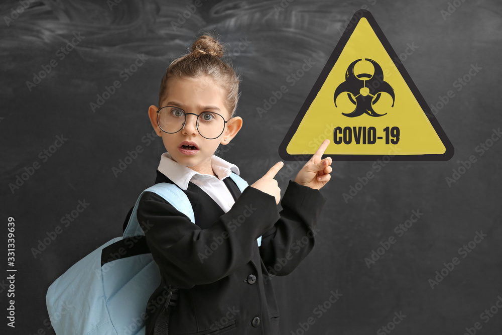 Scared little schoolgirl with warning sign on dark background. Concept of Coronavirus epidemic Scared little schoolgirl with warning sign on dark background. Concept of Coronavirus epidemic