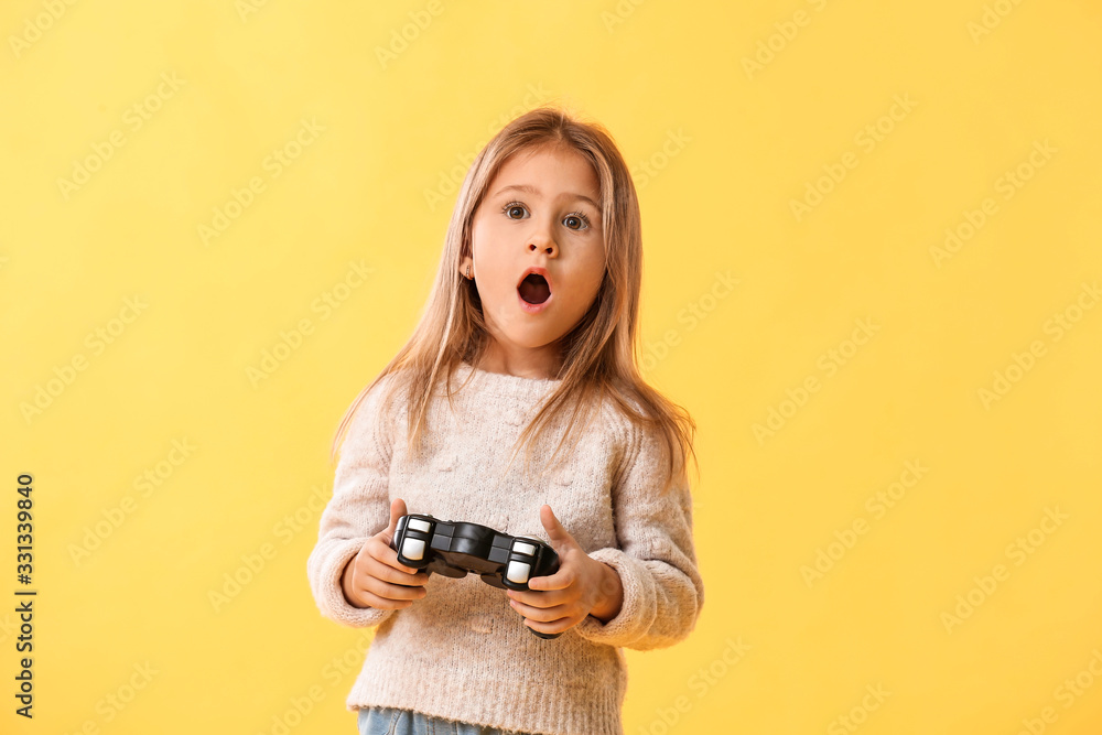 Surprised little girl playing video games on color background Surprised little girl playing video games on color background