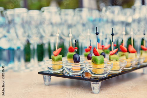 Assorted canapes of fruit and cheese on a glass platter on the background of glasses and champagne. Catering