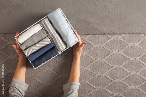 Spring cleaning of closet. Vertical tidying up storage. Neatly folded clothes in the metal white baskets for wardrobe. Grey background. photo