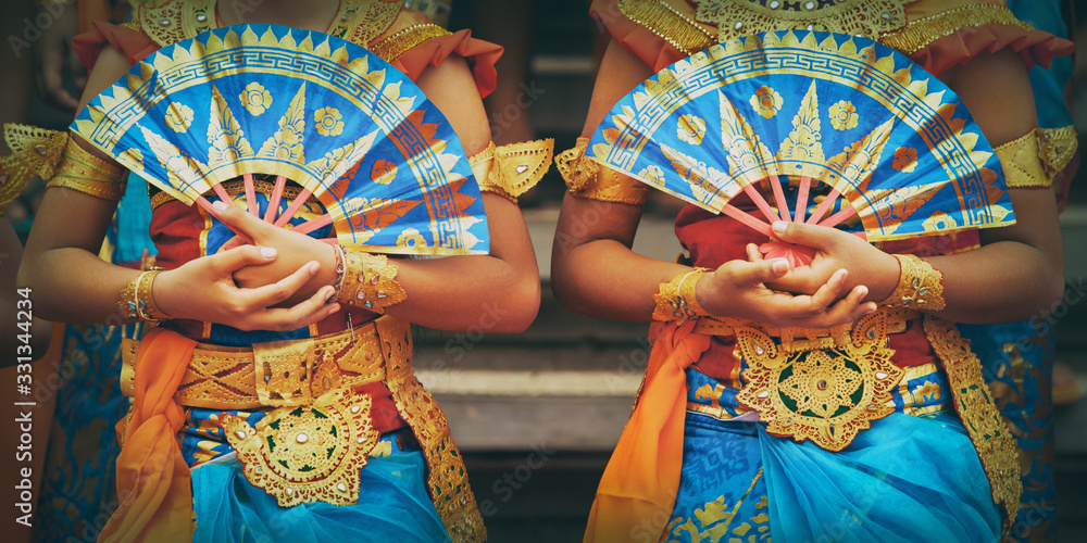 Asian travel background. Group of beautiful Balinese dancer women in traditional Sarong costumes with fans in hands dancing Legong dance. Arts, culture of Indonesian people, Bali island festivals.