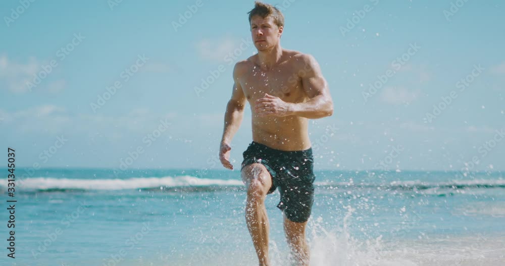 Young attractive muscular man running on the beach in slow motion, baywatch body, beach workout run