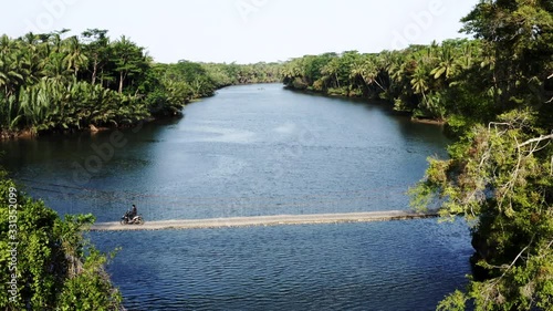 Aerial shot of hanging bridge over the river, guy driving over with scooter Java Indonesia