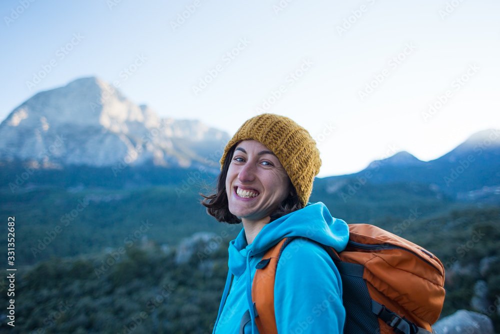 Portrait of a smiling girl with a backpack on a background of mountains.