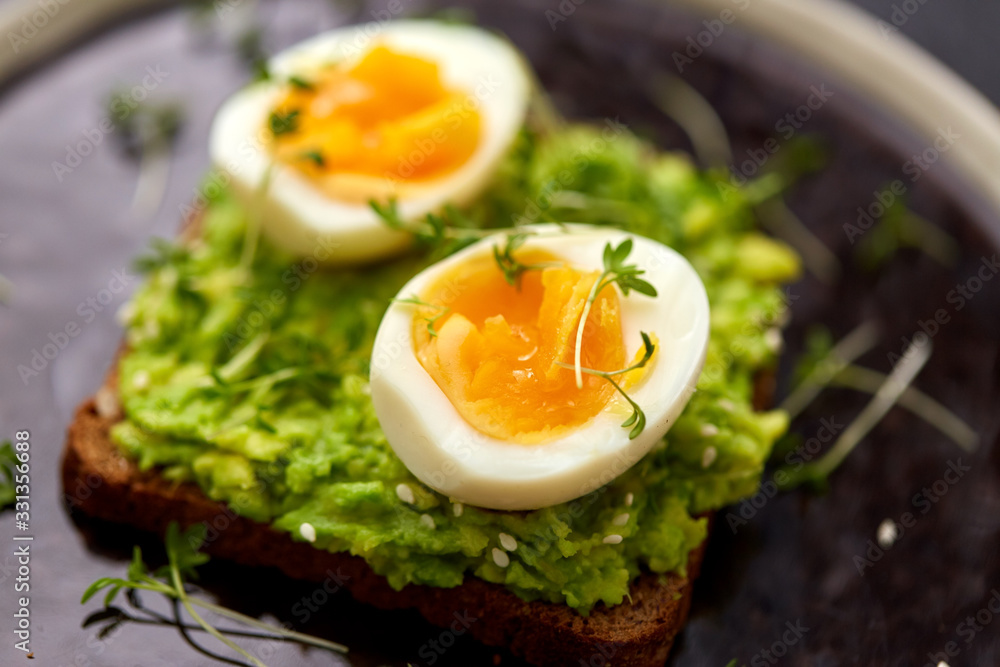 food, eating and breakfast concept - toast bread with mashed avocado, eggs and greens on ceramic plate food, eating and breakfast concept - toast bread with mashed avocado, eggs and greens on ceramic plate