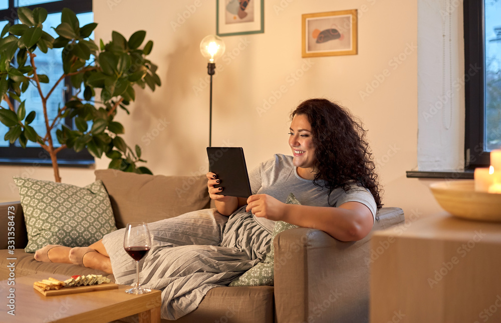 technology, leisure and people concept - happy smiling woman with tablet pc computer, red wine and snacks at home in evening - obrazy, fototapety, plakaty 