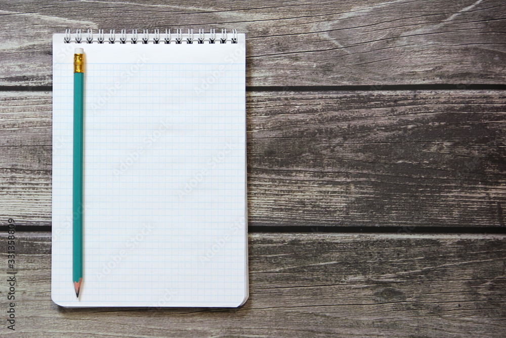 Notepad with a blank white sheet in a checker paper with simple graphite pencil lies on the background of wooden boards. Notepad with a blank white sheet in a checker paper with simple graphite pencil lies on the background of wooden boards.